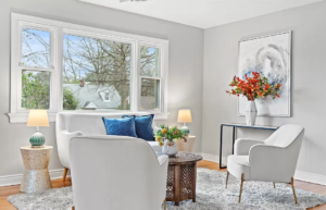 A bright and airy living room with a white sofa, two armchairs, a coffee table, a rug, and a large window.