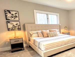 A bedroom with a white bed, large window, rug, lamps, and a painting