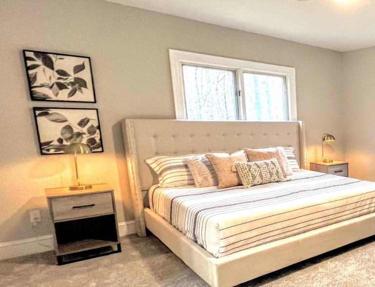 A bedroom with a white bed, large window, rug, lamps, and a painting